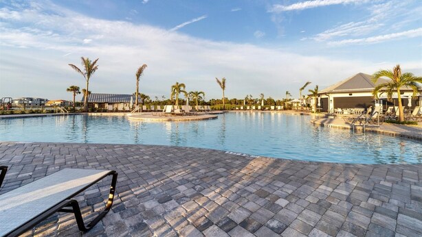 A large swimming pool with lounge chairs and palm trees, surrounded by buildings and a clear sky. - Heritage Landing Golf Club 3 Bedroom Condo 27 Night Minimum 3 Condo (Punta Gorda)