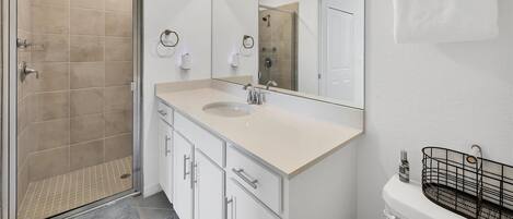 Un baño moderno con ducha, lavamanos con espejo y retrete.