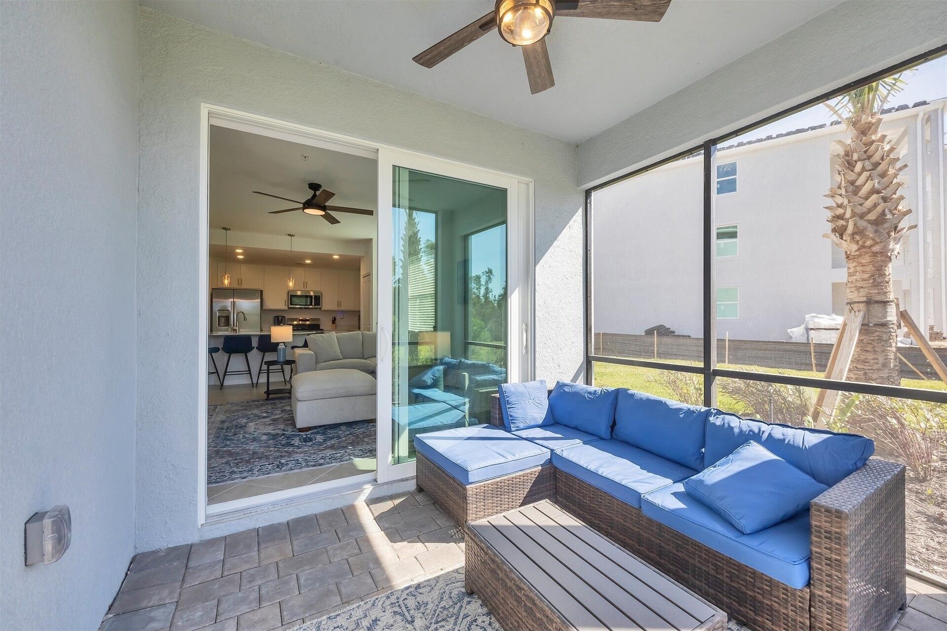 A modern living room with a large window, a ceiling fan, and a wicker sofa with blue cushions.