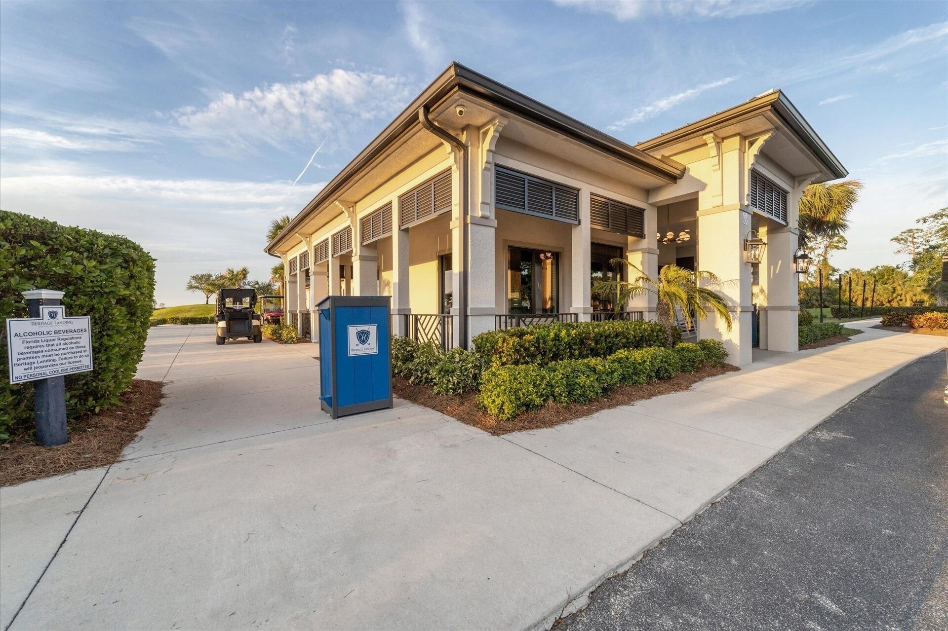 A building with a covered outdoor area, a trash bin, and a sign about alcoholic beverages.