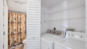 Een wasserette met een wasmachine en droger, een douchegordijn en een witte deur.