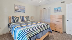 Een slaapkamer met een bed, een dressoir, een kast en twee aan de muur hangende foto's.