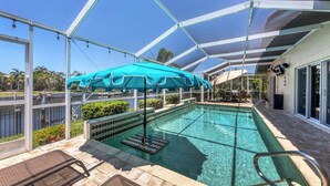 An indoor swimming pool with a glass enclosure, a blue umbrella, and a view of a water body outside. - Family-friendly Waterfront 4br Pool Punta Gorda Isles 4 Bedroom Home (Punta Gorda)