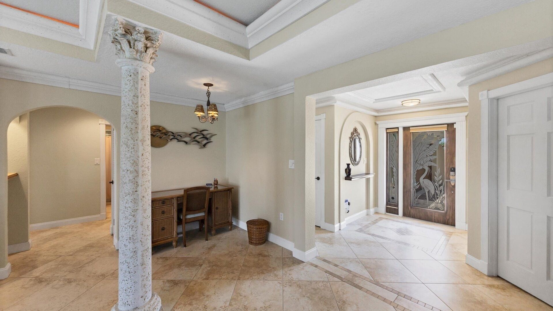A spacious foyer with a high ceiling, a central column, a dining area with a table and chairs, and a decorative wall piece.