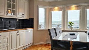 A modern kitchen with white cabinets, a black tiled backsplash, and a dining area with a table and chairs. - Modern villa with sea view in Svanesund | SE09101 (Svanesund)