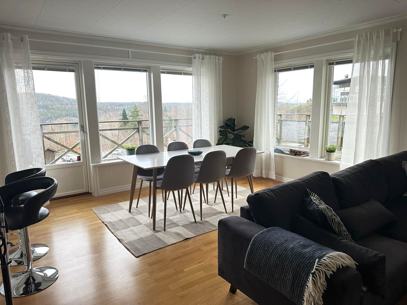 A modern living room with a dining area, large windows, and a view of the outdoors.