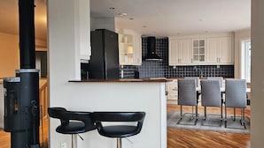 A modern kitchen with white cabinets, a black stove, and a dining area with grey chairs. - Modern villa with sea view in Svanesund | SE09101 (Svanesund)