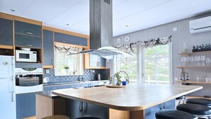 Et moderne køkken med en central ø, barstole, integrerede hårde hvidevarer og udsigt gennem store vinduer.