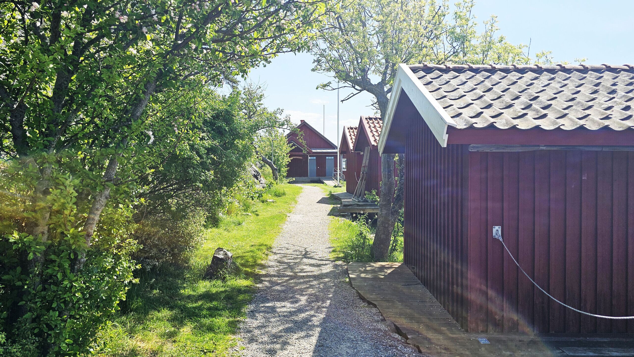 En grussti, der fører hen til en række røde træbygninger med et bølgebliktag.