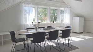 Comedor con una mesa dispuesta para seis personas, sillas negras, techo blanco y ventanas amplias con cortinas.
