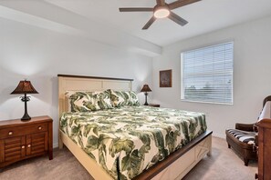 A bedroom with a bed, two nightstands, a ceiling fan, a window with blinds, and a chair. - Heritage Landing Golf Club 30 night minimum 2 Bedroom Condo 2 Condo (Punta Gorda)
