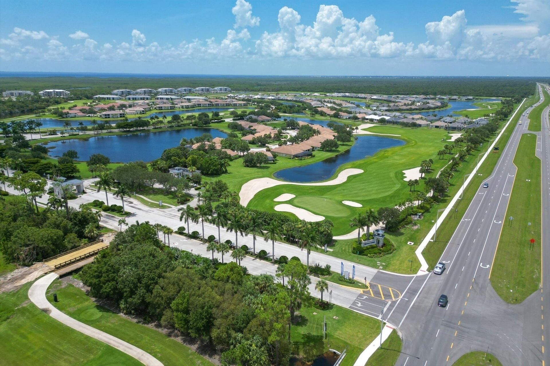 An aerial view of a golf course with multiple ponds, a road, and residential buildings.