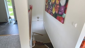 A staircase with a wooden handrail, a colorful floral wall art, and a white door leading to a room with a gray carpet. - Villa with sauna, 650 m to the beach | SE09135 (Varekil)