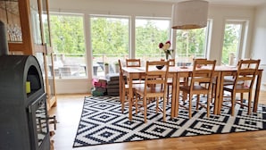 A dining area with a wooden table and chairs, a patterned rug, and a large window with a view of greenery. - Villa with sauna, 650 m to the beach | SE09135 (Varekil)