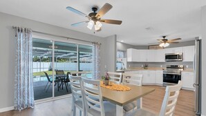 Una cocina moderna con armarios blancos, electrodomésticos de acero inoxidable y un comedor con vista a la piscina.