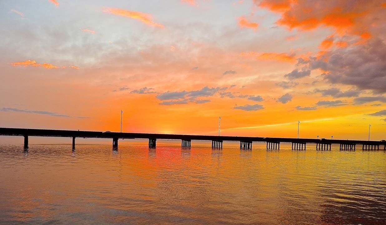 Een pier die zich uitstrekt in kalm water tijdens zonsondergang, met een heldere lucht.