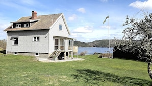 Una casa de dos pisos con balcón, chimenea y vista a un lago.