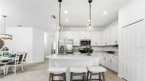 A modern kitchen with white cabinetry, a central island with bar stools, stainless steel appliances, and pendant lighting. - Heritage Landing Resort 30 night minimum 3 Bedroom Condo 3 Condo (Punta Gorda)