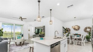 A modern kitchen with a central island, a dining area with white chairs, and a large window overlooking a green landscape. - Heritage Landing Resort 30 night minimum 3 Bedroom Condo 3 Condo (Punta Gorda)