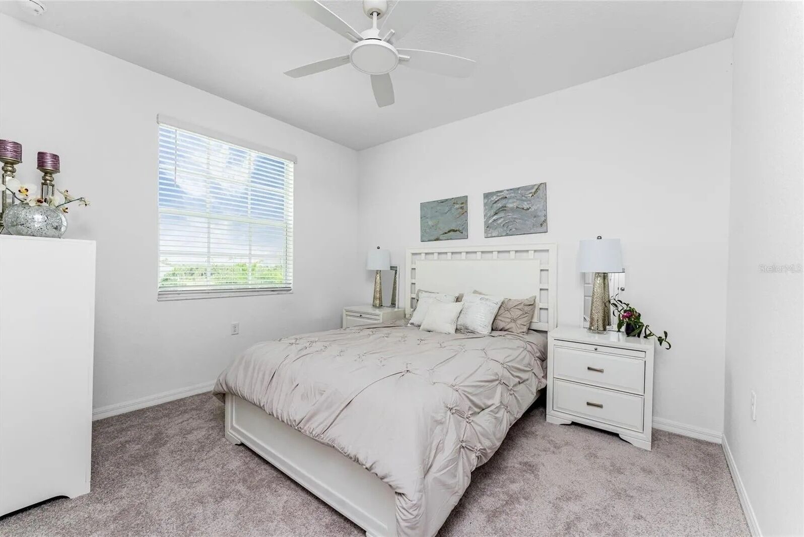 Une chambre à coucher avec un lit, des tables de chevet, un ventilateur de plafond et une fenêtre avec des stores.