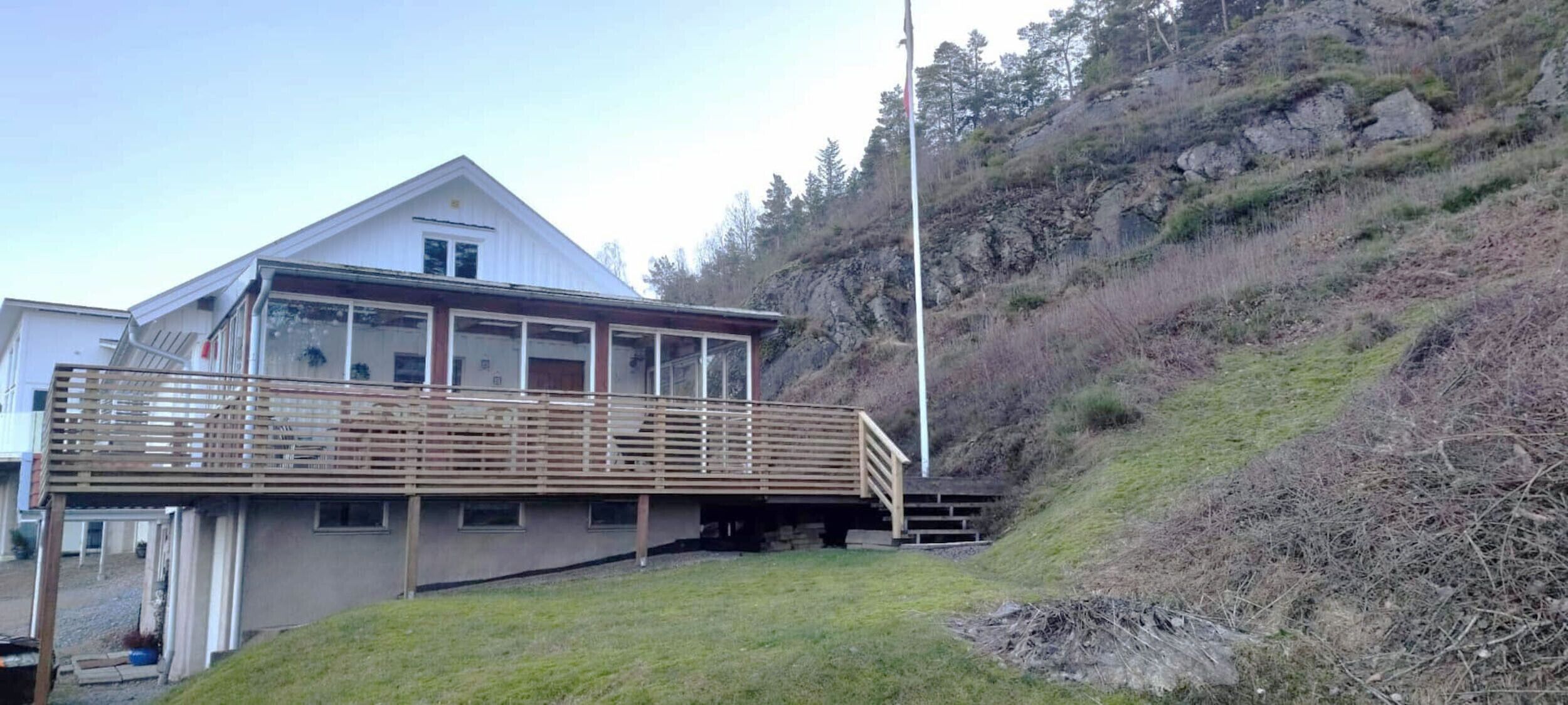 Une maison à deux étages avec un balcon, un petit porche et, en arrière-plan, une pente raide.