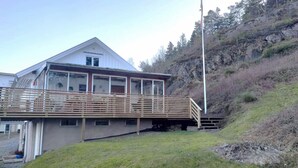 A two-story house with a balcony, a small porch, and a steep hillside in the background. - Stay central & close to the sea in Henån | SE09155 (Henån)