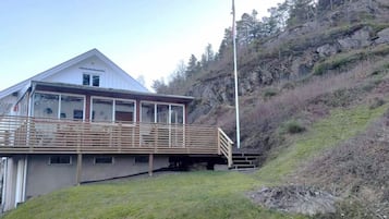 Une maison à deux étages avec un balcon, un petit porche et, en arrière-plan, une pente raide.