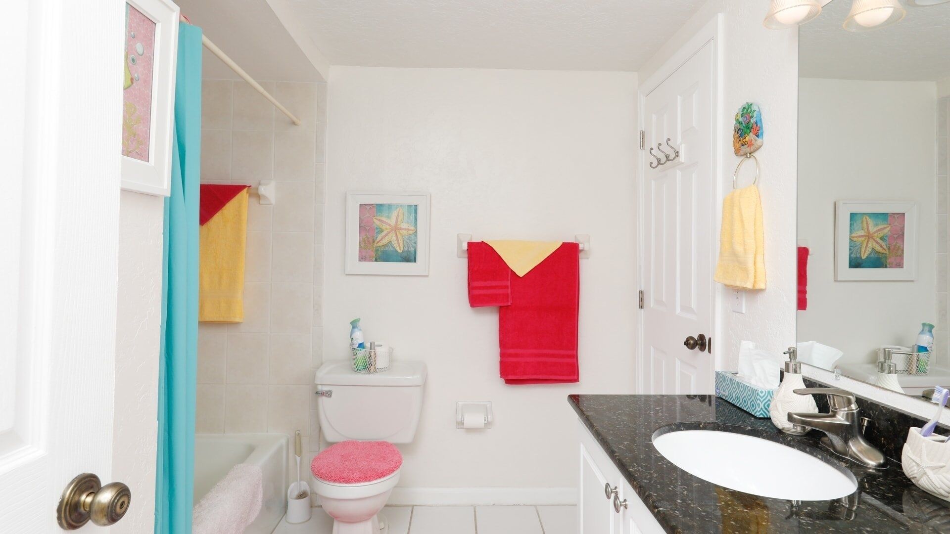 A bathroom with a toilet, sink, and bathtub. There are towels hanging on the wall and a shower curtain.