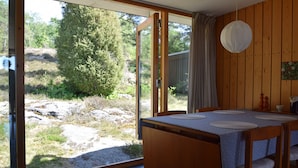 Zona pranzo con tavolo e sedie, vista su un paesaggio naturale attraverso una porta in vetro e pareti in legno.