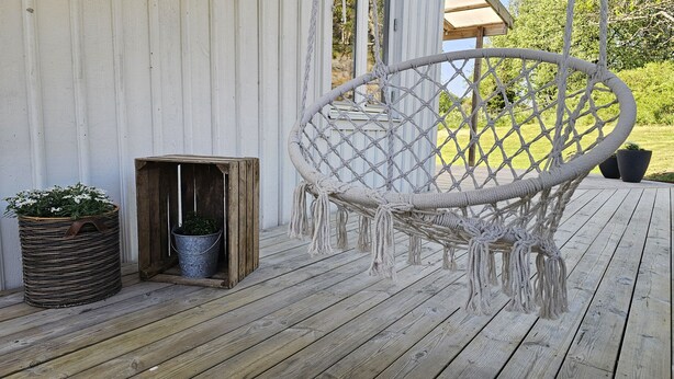 A wooden deck with a macrame chair, a metal bucket planter, and a wooden box with plants. - Charming House near Lysekil & Skaftö | SE09160 (Uddevalla)