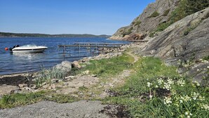 A rocky shoreline with a boat docked on the water, a wooden pier, and a clear view of the distant land. - Charming House near Lysekil & Skaftö | SE09160 (Uddevalla)