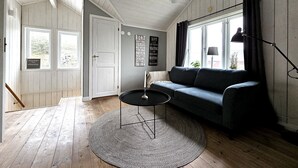 A cozy room with a dark blue sofa, a small black table, and a round rug. There is a window with curtains, a door, and a wall with a poster. - Charming House near Lysekil & Skaftö | SE09160 (Uddevalla)