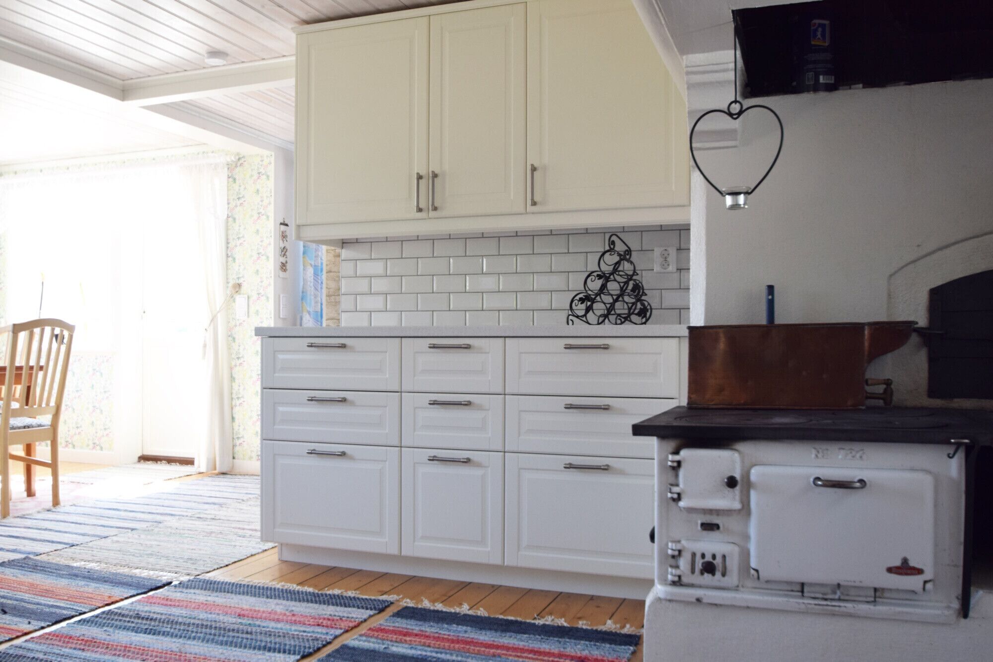 Een keuken met witte kastjes, een betegelde spatwand en een retro fornuis.