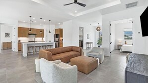 A spacious living area with a large brown sofa, two armchairs, and a coffee table. A kitchen with modern appliances and pendant lighting is visible in the background. - Punta Gorda 3-Bedroom Canalfront Vacation Home with Pool 3 Home (Punta Gorda)