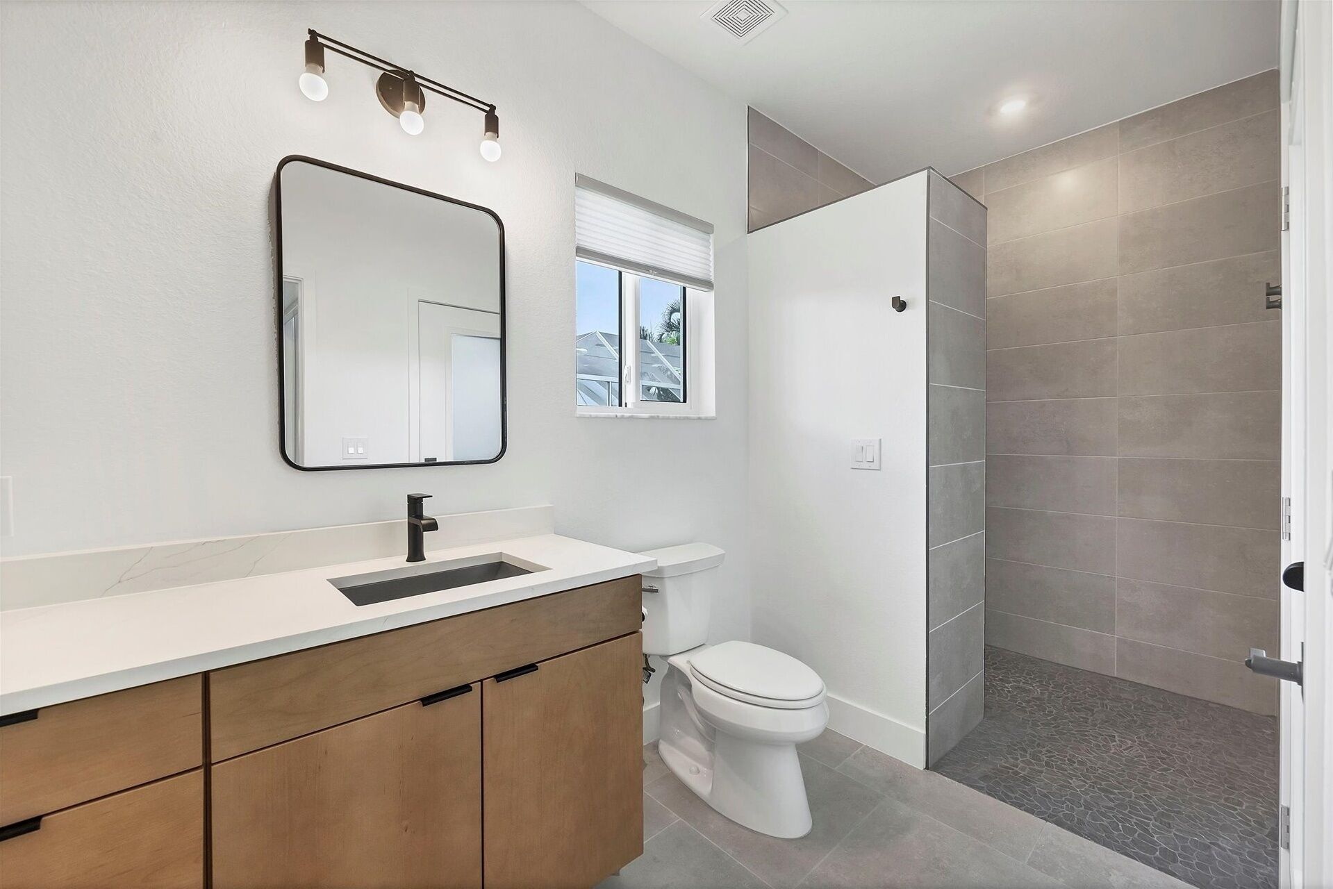 A modern bathroom with a white vanity, a large mirror, a toilet, and a shower area.