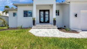 A modern two-story house with a black front door, large windows, and a paved driveway leading to the entrance. - Punta Gorda 3-Bedroom Canalfront Vacation Home with Pool 3 Home (Punta Gorda)