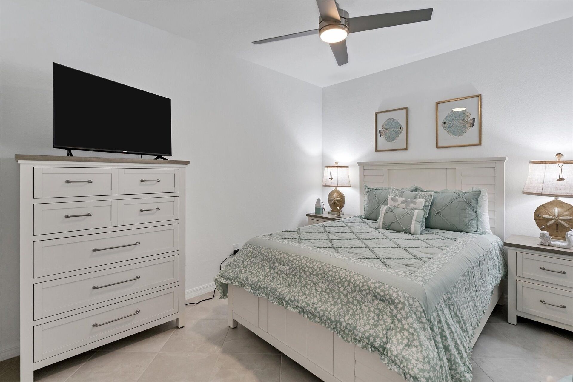 A bedroom with a bed, a dresser, a TV, two wall art pieces, and a ceiling fan.