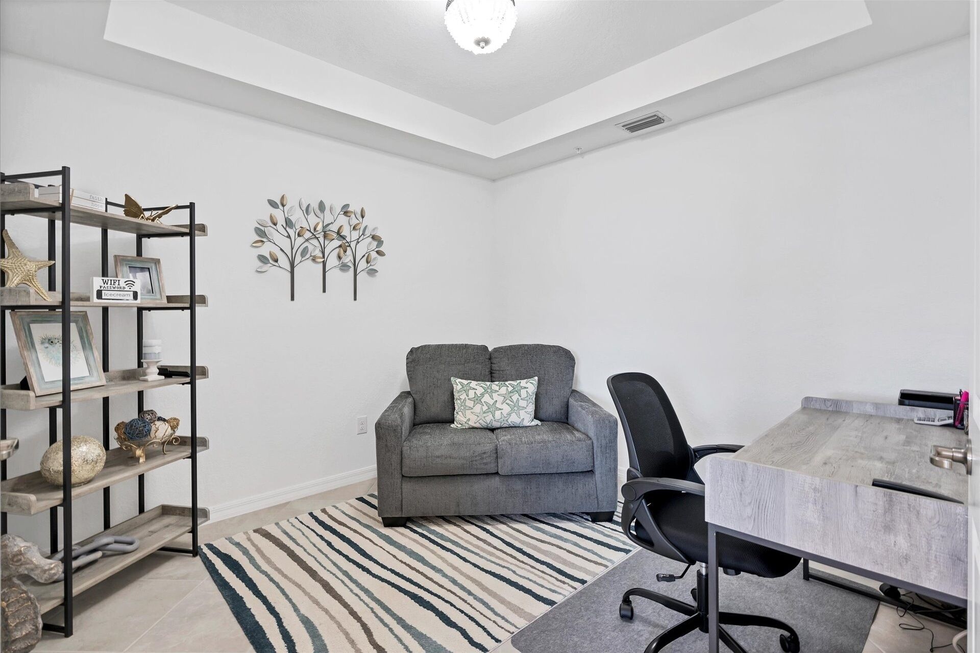 A modern, minimalist room with a grey sofa, a black office chair, a wooden side table, and a striped rug.