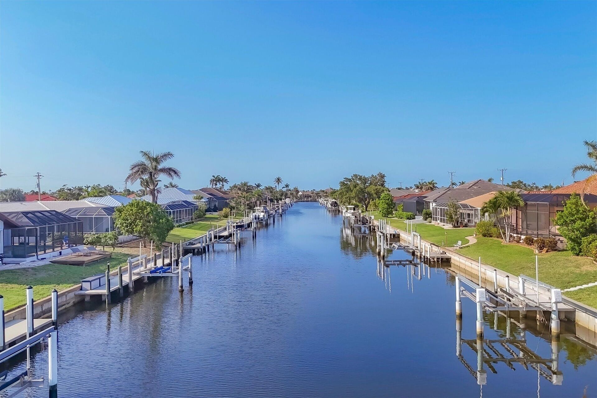A canal lined with houses and docks, reflecting the buildings and palm trees.