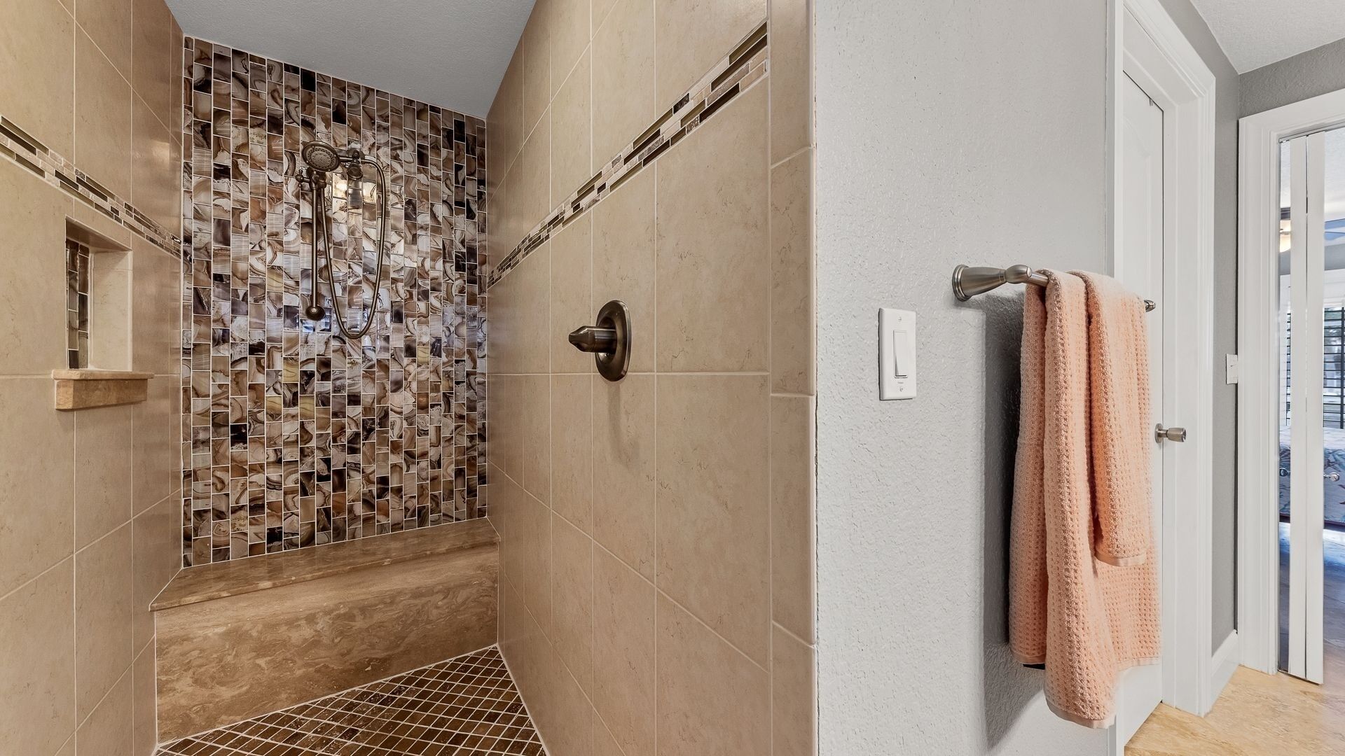 Une salle de bain avec un mur de douche recouvert de mosaïques, un porte-serviettes avec une serviette et une porte de douche.