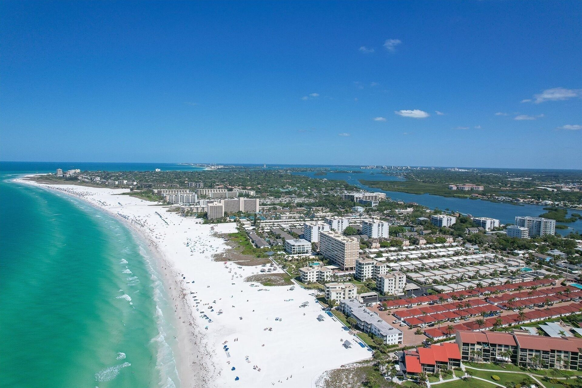 An aerial view of a coastal area with a beach, hotels, and a marina.