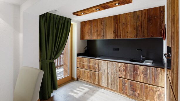 A modern kitchen with wooden cabinets, a black countertop, and a window with a green curtain. - Apartment 'Monte Vago' with Mountain View, Balcony and Wi-Fi (Livigno)