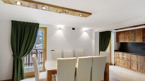 A dining area with a wooden table and chairs, a kitchen with wooden cabinets, and a balcony with a view. - Apartment 'Monte Vago' with Mountain View, Balcony and Wi-Fi (Livigno)