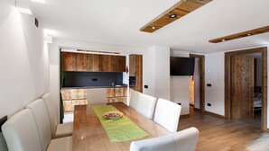 A dining area with a wooden table, white chairs, and a green placemat. - Apartment 'Monte Vago' with Mountain View, Balcony and Wi-Fi (Livigno)