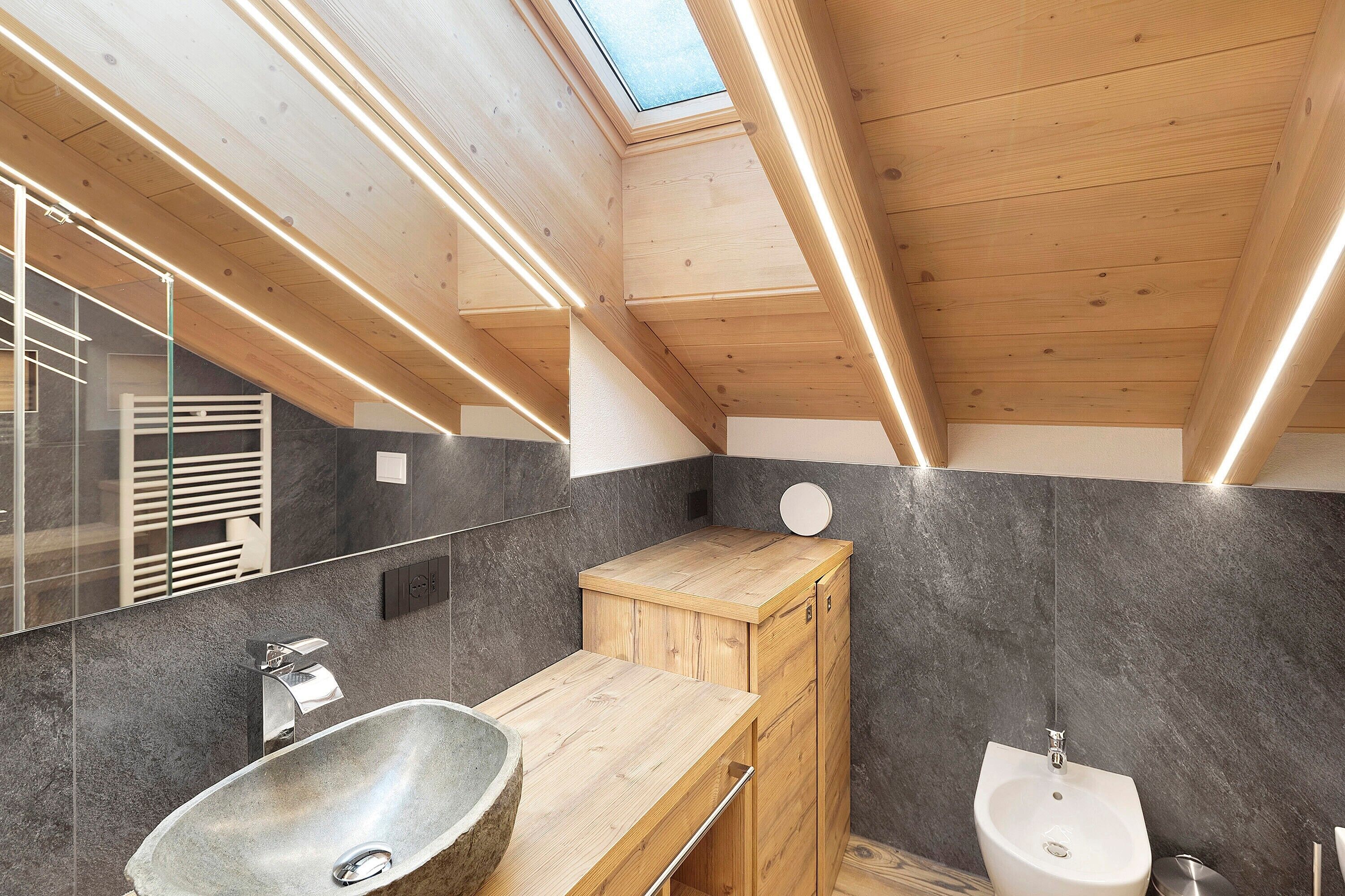 A modern bathroom with a skylight, wooden cabinetry, a large sink, and a bidet.