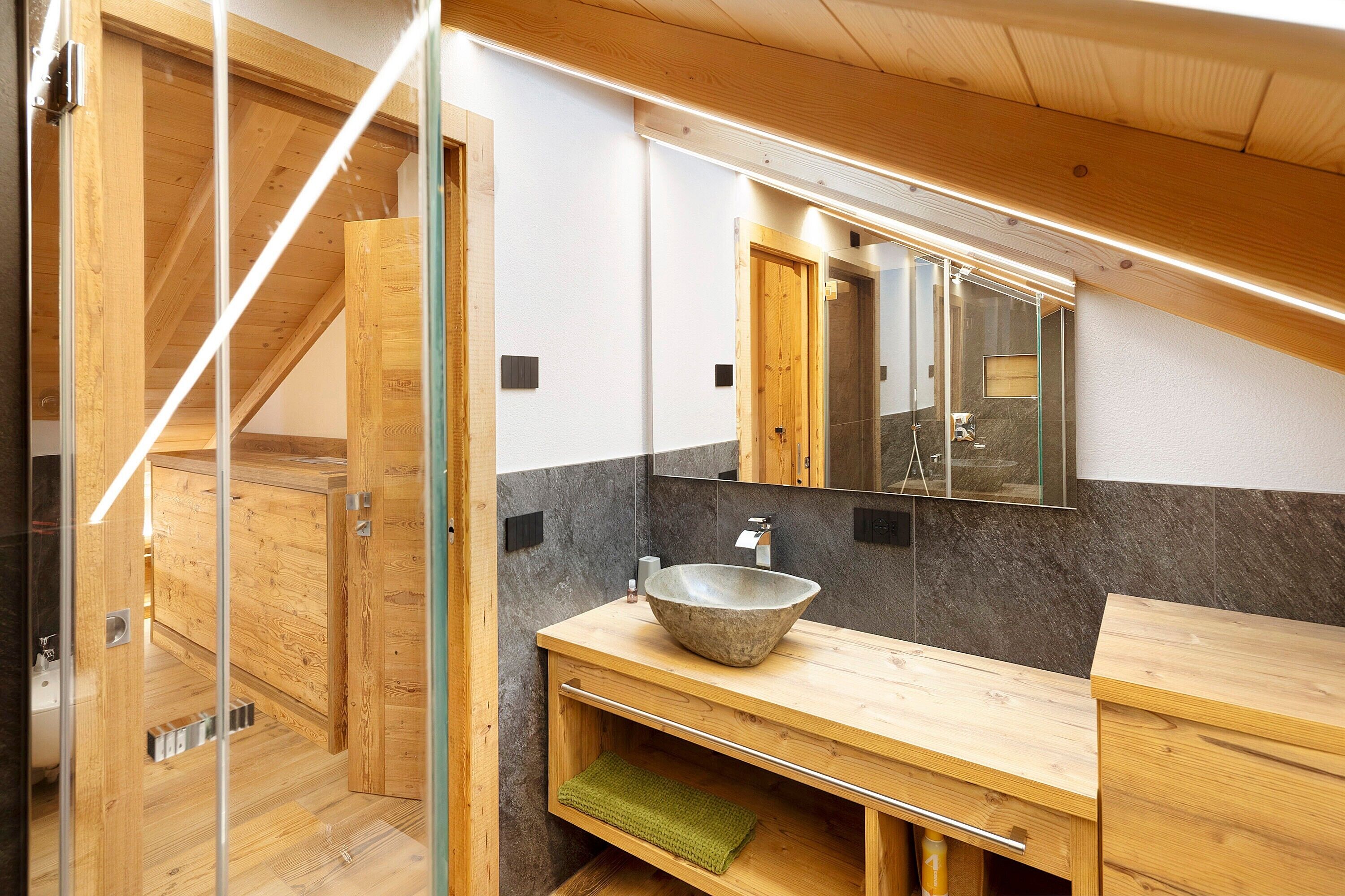 Un baño moderno con tocador de madera, un espejo grande y un lavabo de piedra.
