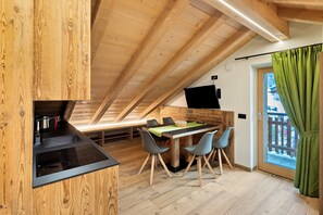 A modern kitchen with a wooden ceiling, a dining area with a table and chairs, and a view through a glass door. - Mansarda Rin Da Gen Apartment with Mountain View, Balcony and Wi-Fi (Livigno)