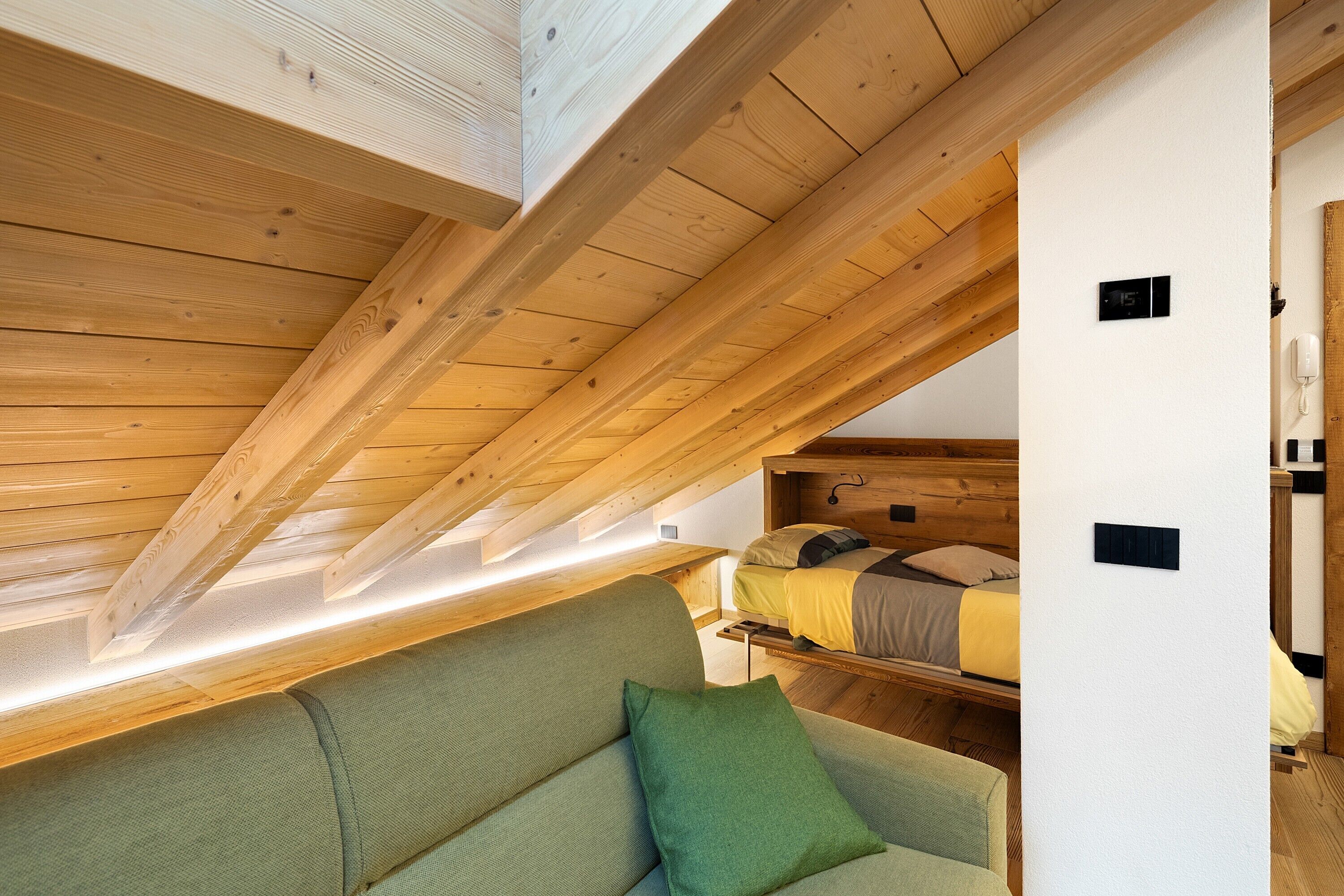 A room with a loft bed, a sofa, and a wooden ceiling.