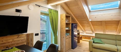A loft-style room with a dining area, a sofa, a TV, and a wooden ceiling.