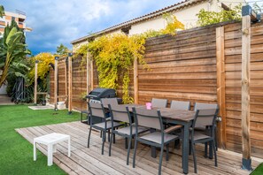 Eine Holzterrasse mit Tisch, Stühlen, einem Grill und einem Holzzaun mit Kletterpflanzen.